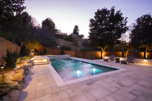 Geometric pool with stone decking lit at dusk