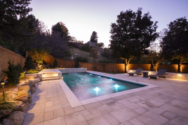 Geometric pool with stone decking lit at dusk